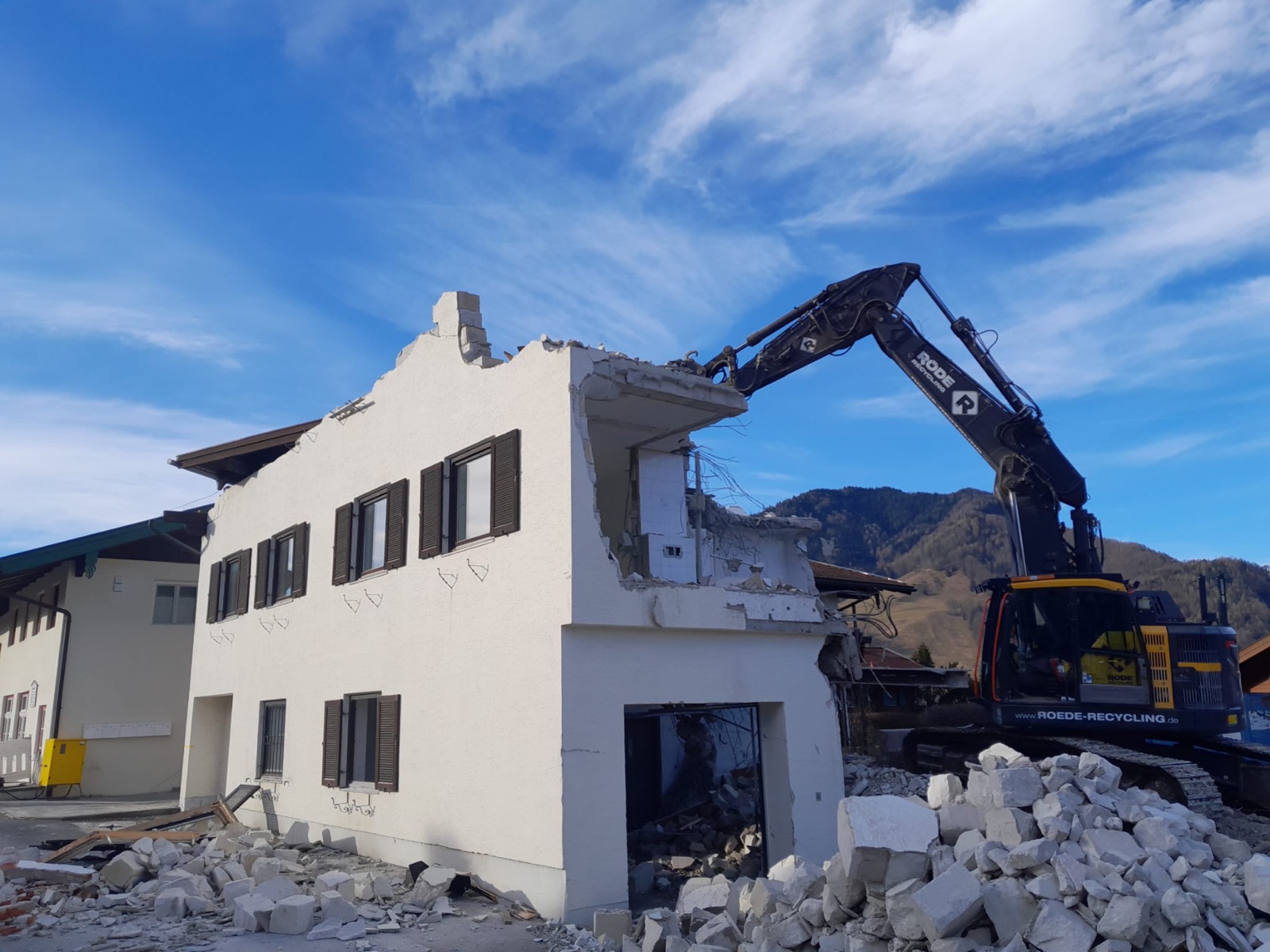 Gebäudeabbruch mit Röde-Bagger vor Bergkulisse