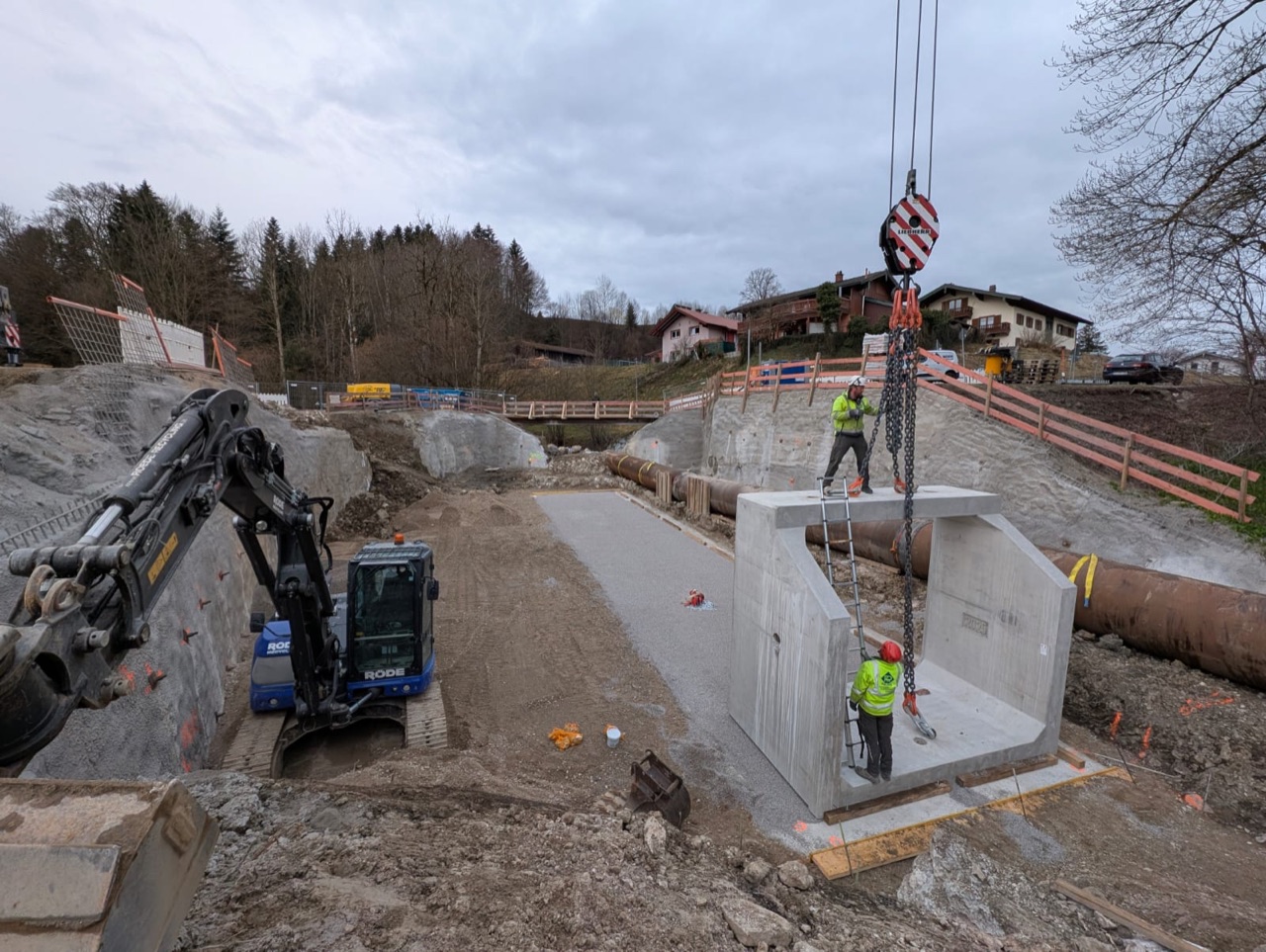Tiefbau-Bagger und Kran beim Setzen eines Betondurchlasses